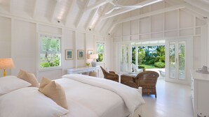 A spacious bedroom with a large bed, a desk, and wicker chairs. - The Great House | Beach Front - Located in  Exquisite St. Peter with Private Pool (Mullins)