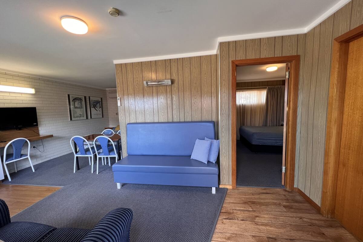 Un espace de vie compact avec un canapé bleu, un petit coin repas avec des chaises, un téléviseur et un mur d’accent en bois.