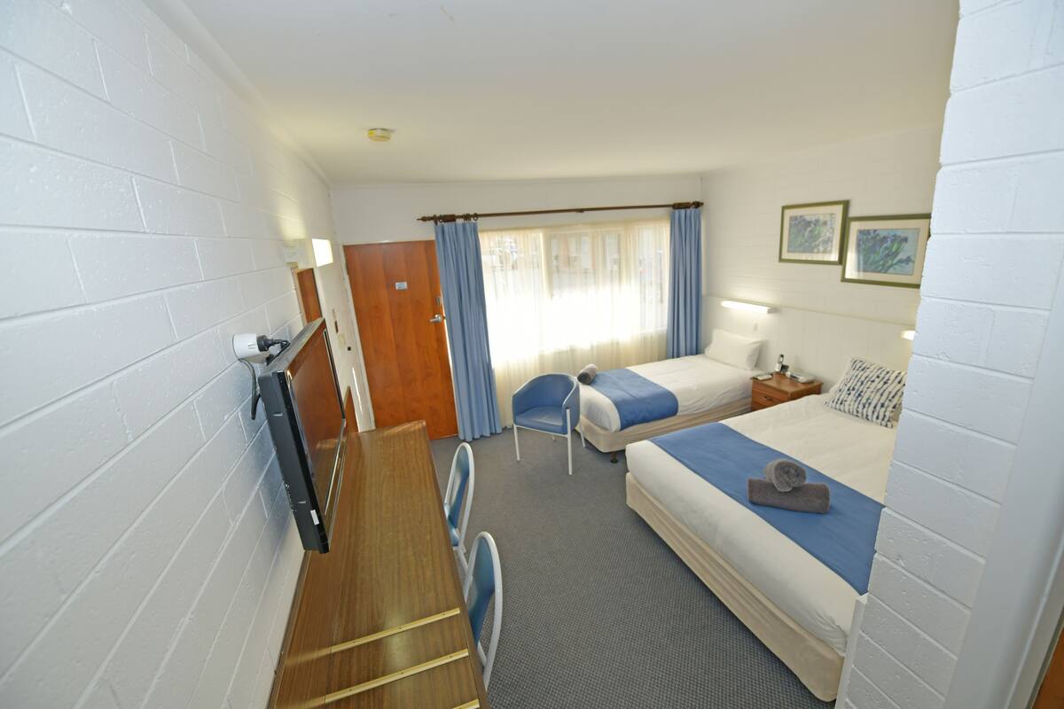 Une chambre d’hôtel comprenant un lit, un bureau, une chaise, une fenêtre avec des rideaux et un téléviseur fixé au mur.