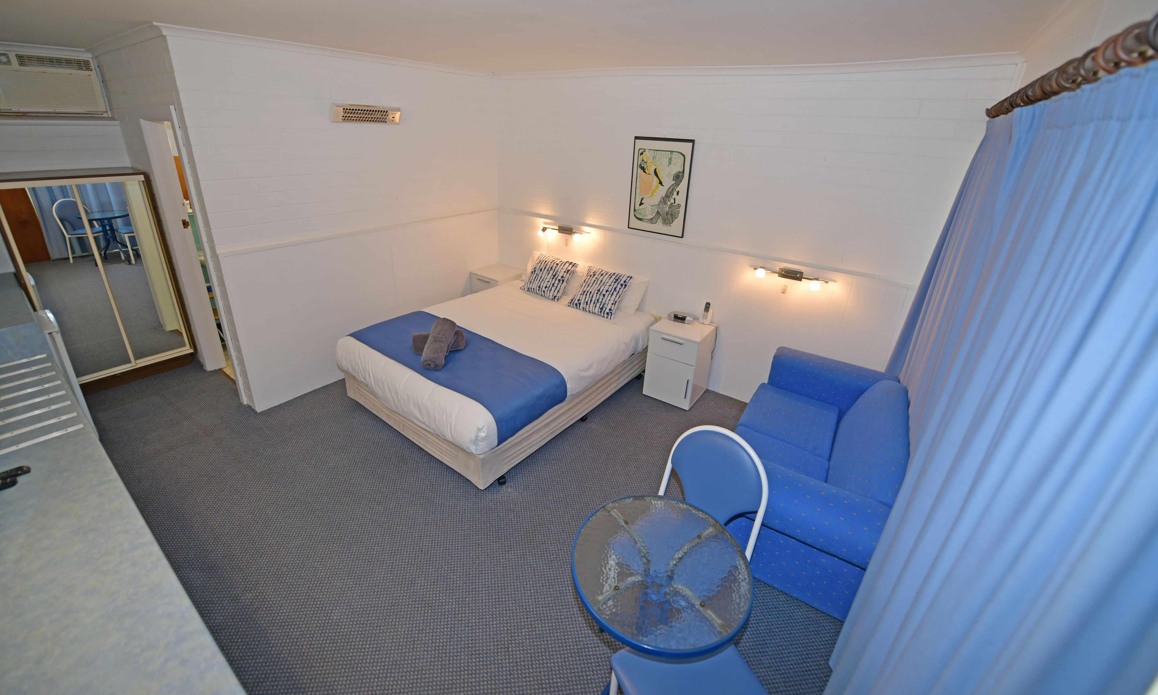 Une chambre d’hôtel de taille réduite, comprenant un lit simple, une petite table de chevet, une chaise et une table en verre.