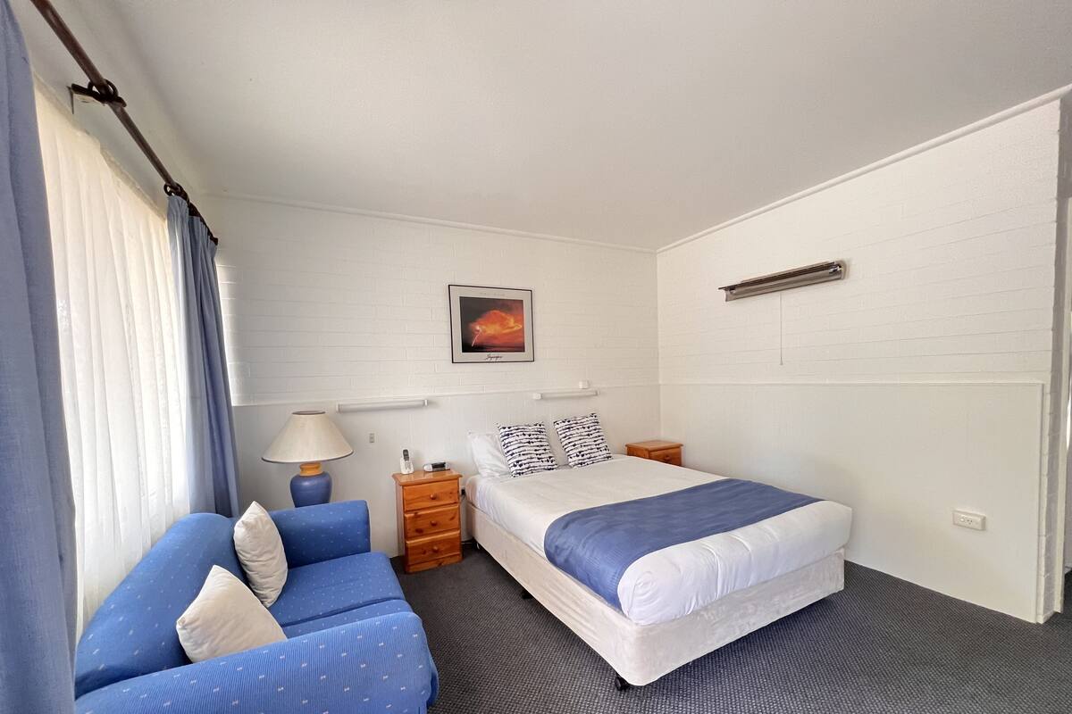 Une chambre d’hôtel avec un lit, un canapé, une table de chevet, une lampe et un tableau au mur.