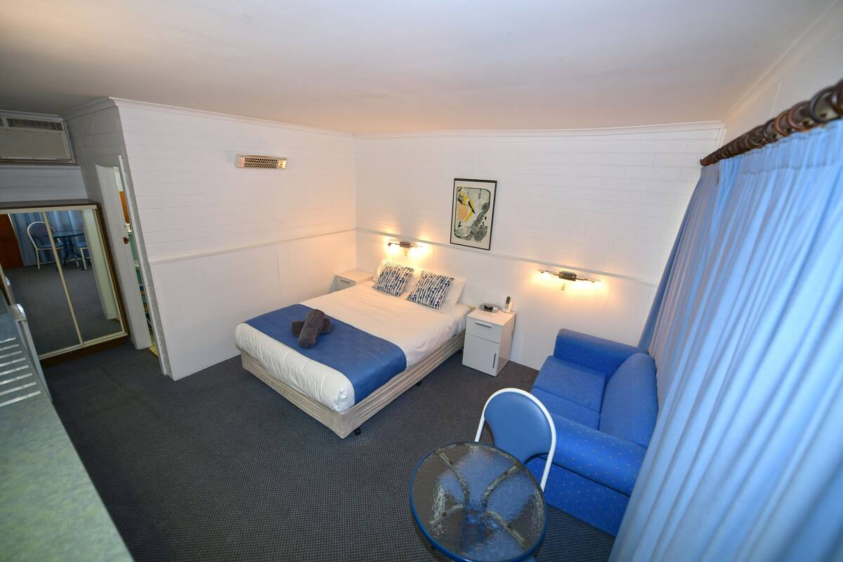 Une chambre d’hôtel avec un lit, une table de chevet, une chaise et une petite table.