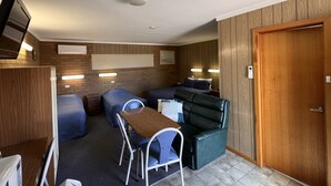 A compact room with a kitchenette, a dining area with a table and chairs, a sofa, and a wooden door.
