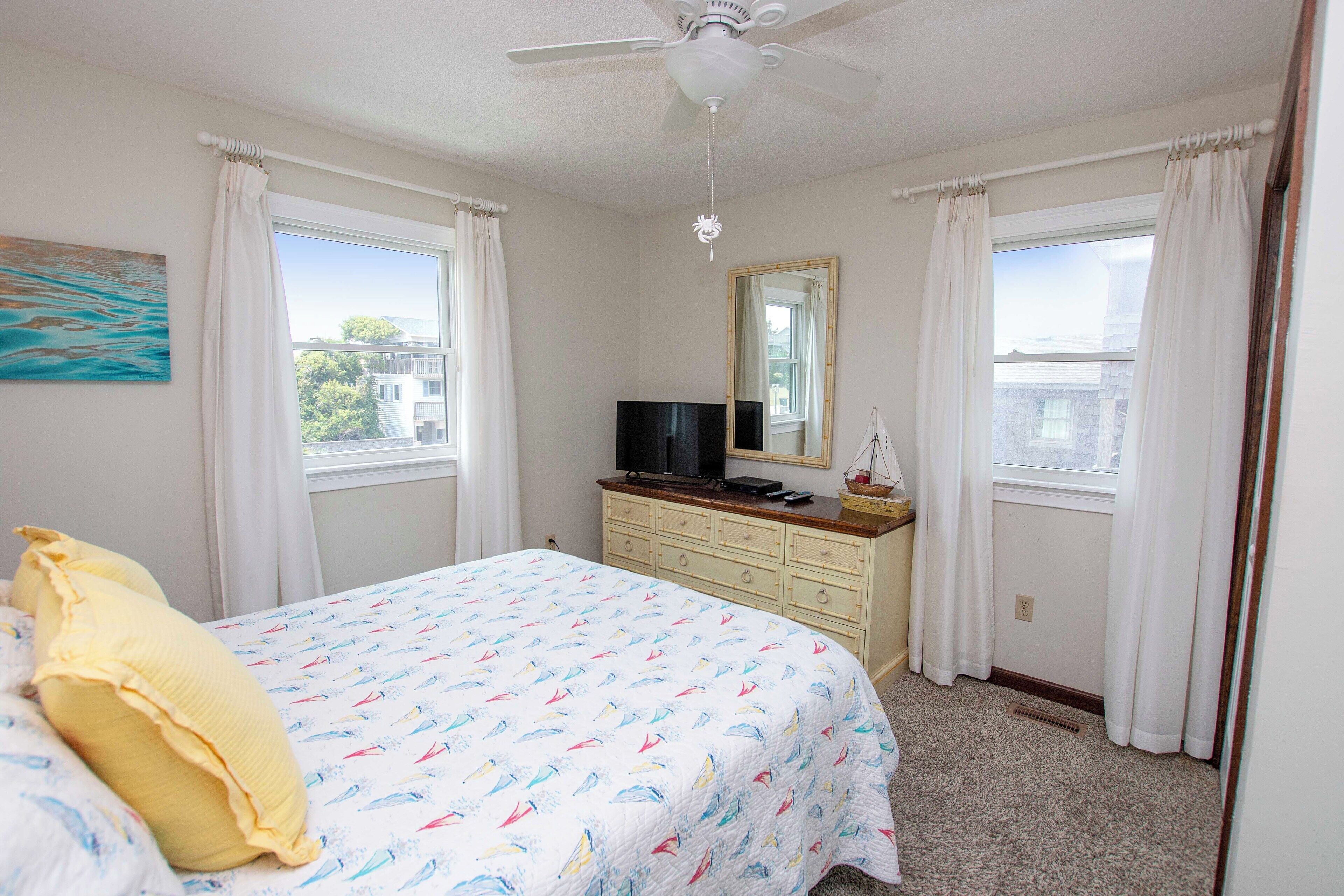 A bedroom with a bed, a dresser, a television, and a ceiling fan.