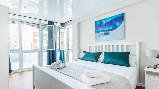 Une chambre d’hôtel moderne avec un grand lit, du linge de lit blanc, des coussins turquoise et un tableau représentant les aurores boréales.
