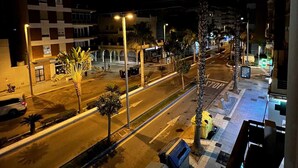 Une vue nocturne d’une rue, avec un bâtiment dont la façade est ornée d’un motif à carreaux, des lampadaires et un passage piéton.