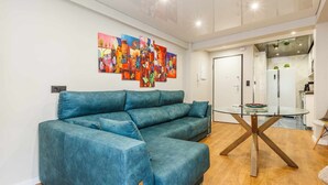 Un salon moderne avec un canapé d’angle bleu, une table basse en verre et un tableau abstrait aux couleurs vives accroché au mur.