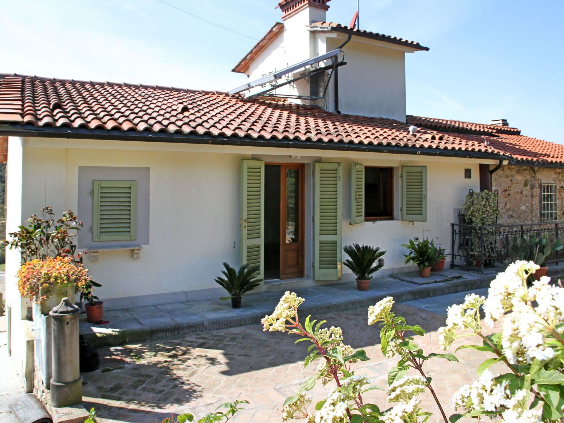 A traditional Mediterranean-style house with a tiled roof, green shutters, and potted plants.