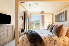 A bedroom with a bed, a TV, a ceiling fan, a window with curtains, and a view of the outdoors. - Luxury Townhome, Theater & Family Room, Hot Tub! 2 Masters (Kamas)