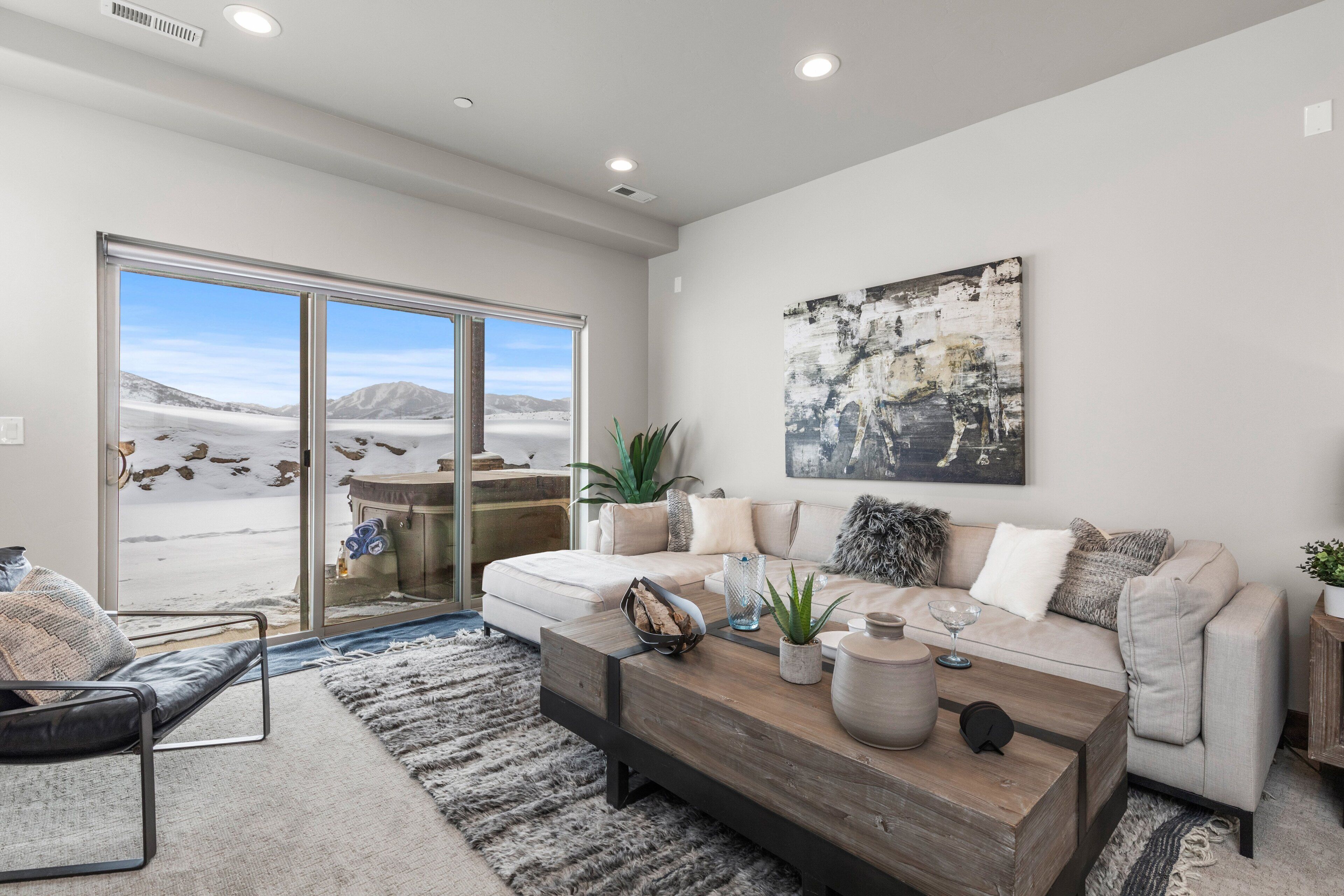 Ein modernes Wohnzimmer mit einer Couch, einem Couchtisch und einem großen Fenster mit Blick auf eine verschneite Landschaft.