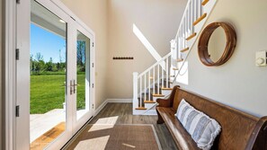 A hallway with a wooden bench, a staircase, and a view of a green lawn.