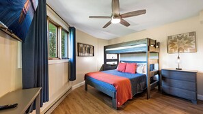 Une chambre avec un lit superposé, un bureau, une chaise, un ventilateur de plafond et une fenêtre avec des rideaux.