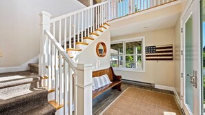 A staircase with white railings and wooden steps, a bench with a striped cushion, a window with a view of greenery, and an American flag on the wall.