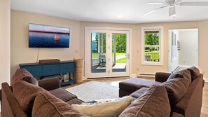 Sala de estar com televisão, um armário azul, sofás marrons e vista para um deck externo através de portas de vidro.