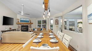 A spacious living room with a fireplace, a dining area set for four, and large windows offering a view of the outdoors.