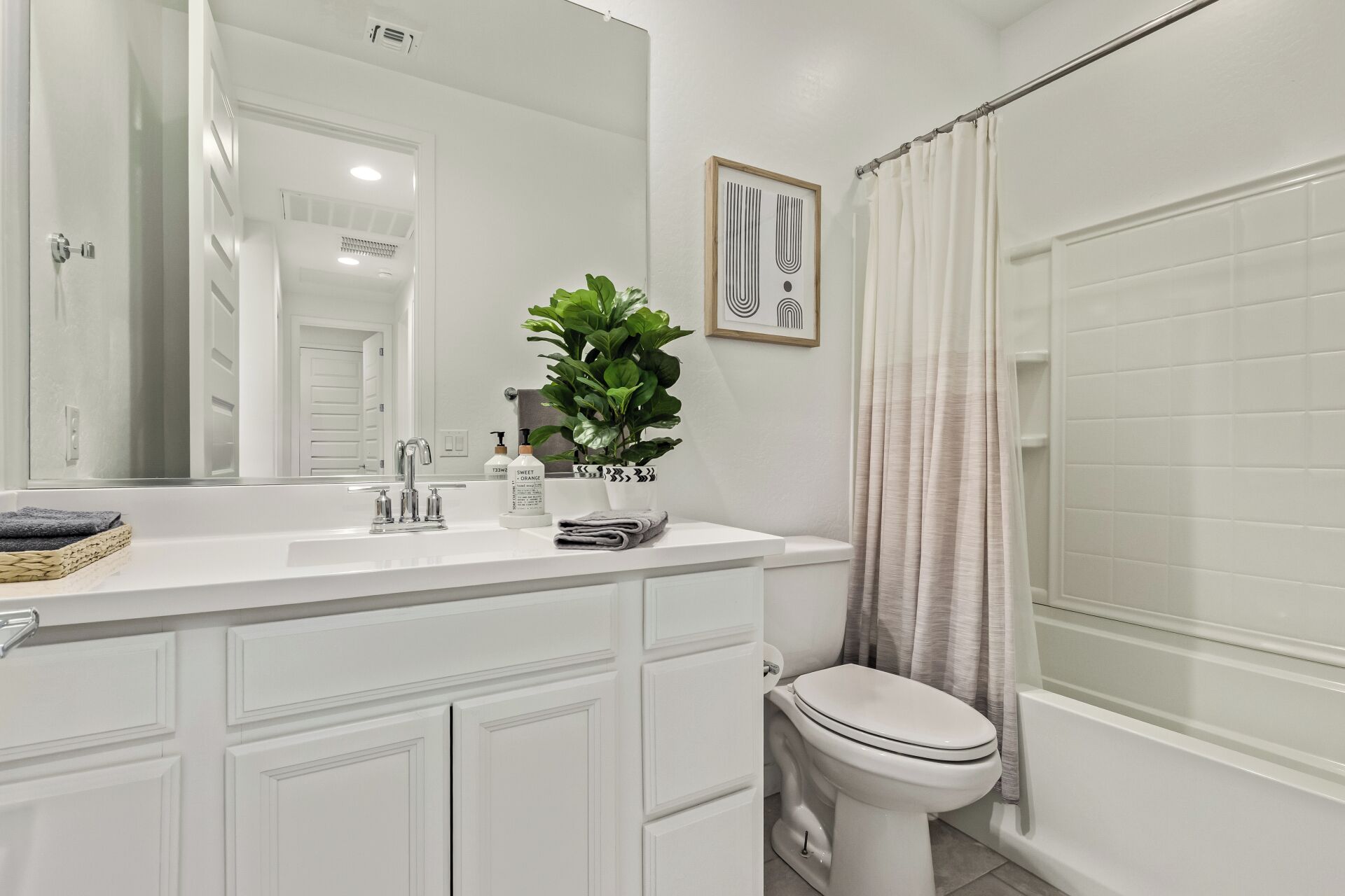 A modern bathroom with a white vanity, a large mirror, a potted plant, and a shower curtain.
