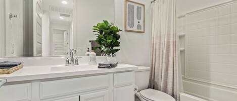 A modern bathroom with a white vanity, a large mirror, a potted plant, and a shower curtain.