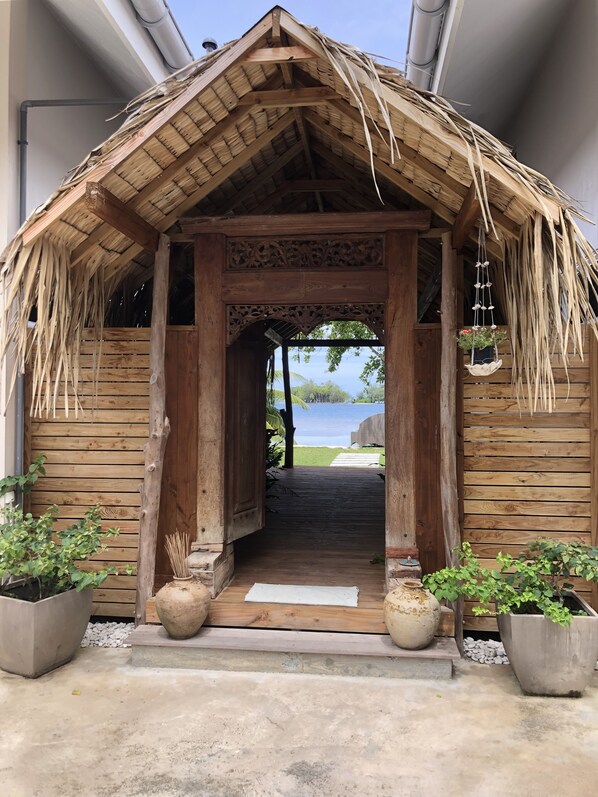 Une structure en bois surmontée d’un toit de chaume, agrémentée d’une arche décorative et de plantes en pot.