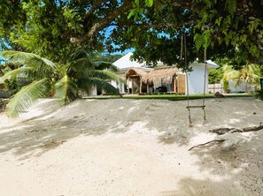 Une zone sablonneue avec une structure à toit de chaume et des palmiers.