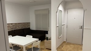 A room with a white table, two chairs, a dark brown sofa, a small potted plant, and a white door with a decorative archway. - Casa Oceano - 2 Bedroom Apartment (San Fernando)