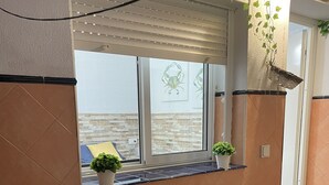 A wooden bench with a slatted backrest, positioned in front of a window with a view of a brick wall and a door. - Casa Oceano - 2 Bedroom Apartment (San Fernando)