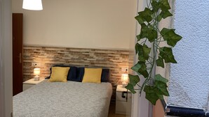 A bedroom with a bed, two bedside lamps, a wall-mounted shelf, and a potted plant. - Casa Oceano - 2 Bedroom Apartment (San Fernando)