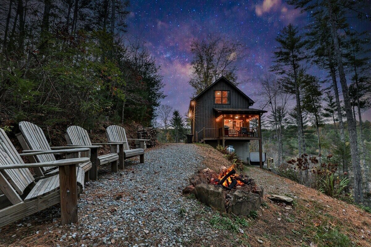 A cabin with a deck, a fire pit, and a starry night sky.