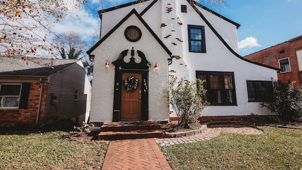Une maison blanche avec une porte marron et un chemin de briques menant à l’entrée.