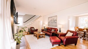 Un salon spacieux avec un escalier, des canapés en cuir, une table basse et un coin repas avec des chaises en bois.