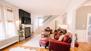Un salon spacieux doté d’une cheminée, d’un canapé en cuir rouge, d’un plancher en bois et d’un escalier menant à un autre niveau.