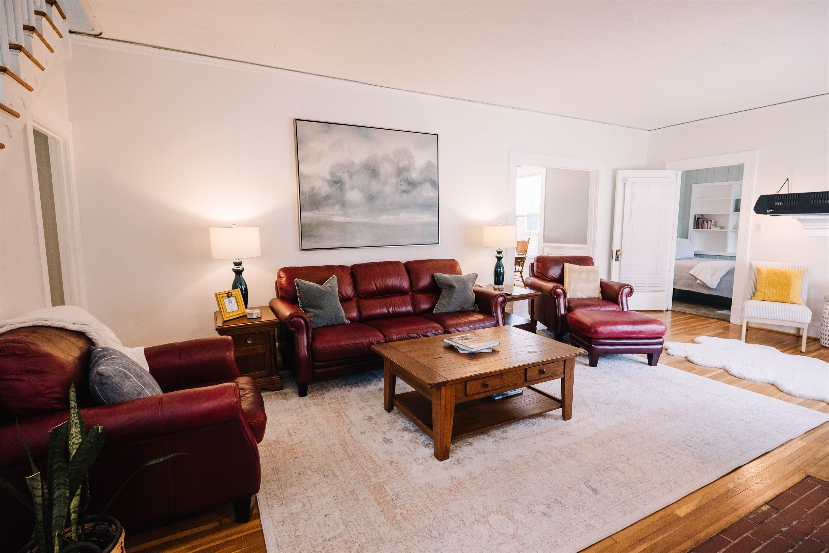A living room with a red leather sofa, a wooden coffee table, and a painting on the wall.