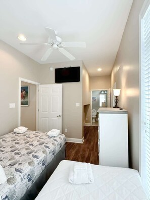 A bedroom with two beds, a ceiling fan, a TV, and a bathroom visible through an open door.