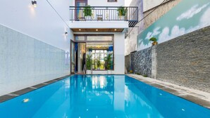 A swimming pool with a view of a building with a balcony and plants. - Gió Chiều Homestay - Riverside & Swimming pool (Hội An)