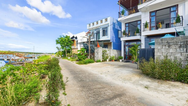 A modern hotel with a concrete pathway leading to the entrance, surrounded by lush greenery and a clear blue sky. - Gió Chiều Homestay - Riverside & Swimming pool (Hội An)