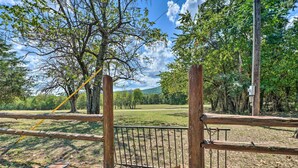 Un área cercada con valla metálica y postes de madera, rodeada de árboles y un campo cubierto de césped.