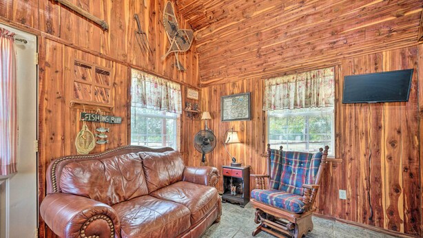 Una habitación acogedora con paredes de madera, un sofá de cuero, un sillón escocés, un televisor y un ventilador.