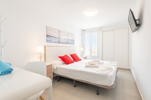 A hotel room with a bed, a desk, a chair, a TV mounted on the wall, and a window with a view.