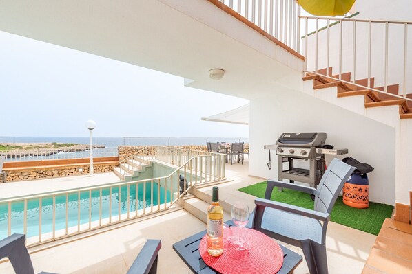 A balcony with a pool, a grill, and a table with a bottle and glass.