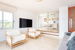 A living room with two wicker chairs, a sofa, a flat-screen TV, and a dining area with a table and chairs. - Villa Enderrosall in Porto Cristo (Porto Cristo)
