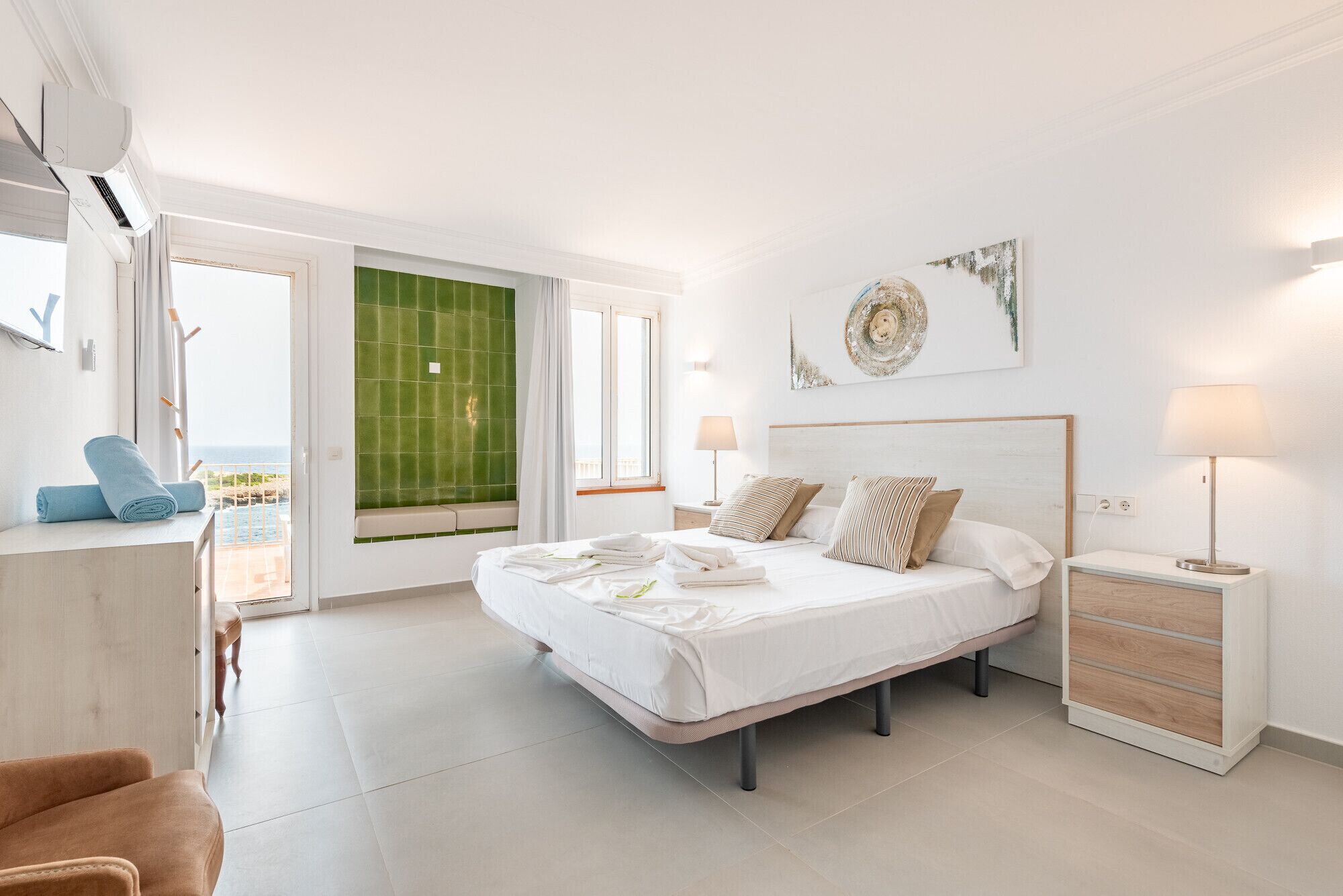 Een moderne slaapkamer met een bed, nachtkastjes, een stoel en uitzicht op zee.