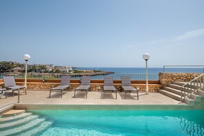 A pool area with lounge chairs and a view of the sea.