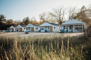 Une rangée de cabanes blanches, chacune dotée d’une véranda, entourée d’herbes hautes et d’arbres.
