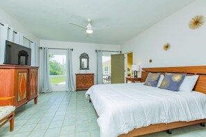 Um quarto espaçoso com uma cama grande, cabeceira de madeira, ventilador de teto e vista para o exterior através de uma porta de correr.