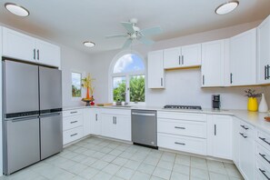 Uma cozinha moderna com armários brancos, eletrodomésticos de aço inoxidável e uma grande janela que traz luz natural.