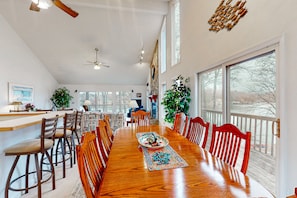 Enjoy meals in this dining area with a long table and comfortable chairs, surrounded by large windows offering views of the outdoors.