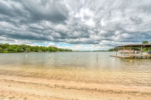 Enjoy a serene lakeside retreat with a clear view of the water, sandy beach, and a dock with a covered seating area.