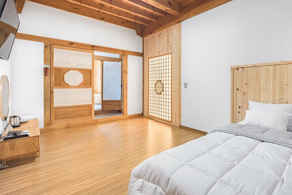 Un dormitorio con cabecera de madera, cama con ropa de cama blanca, suelo de madera y una puerta corredera con diseño tradicional.