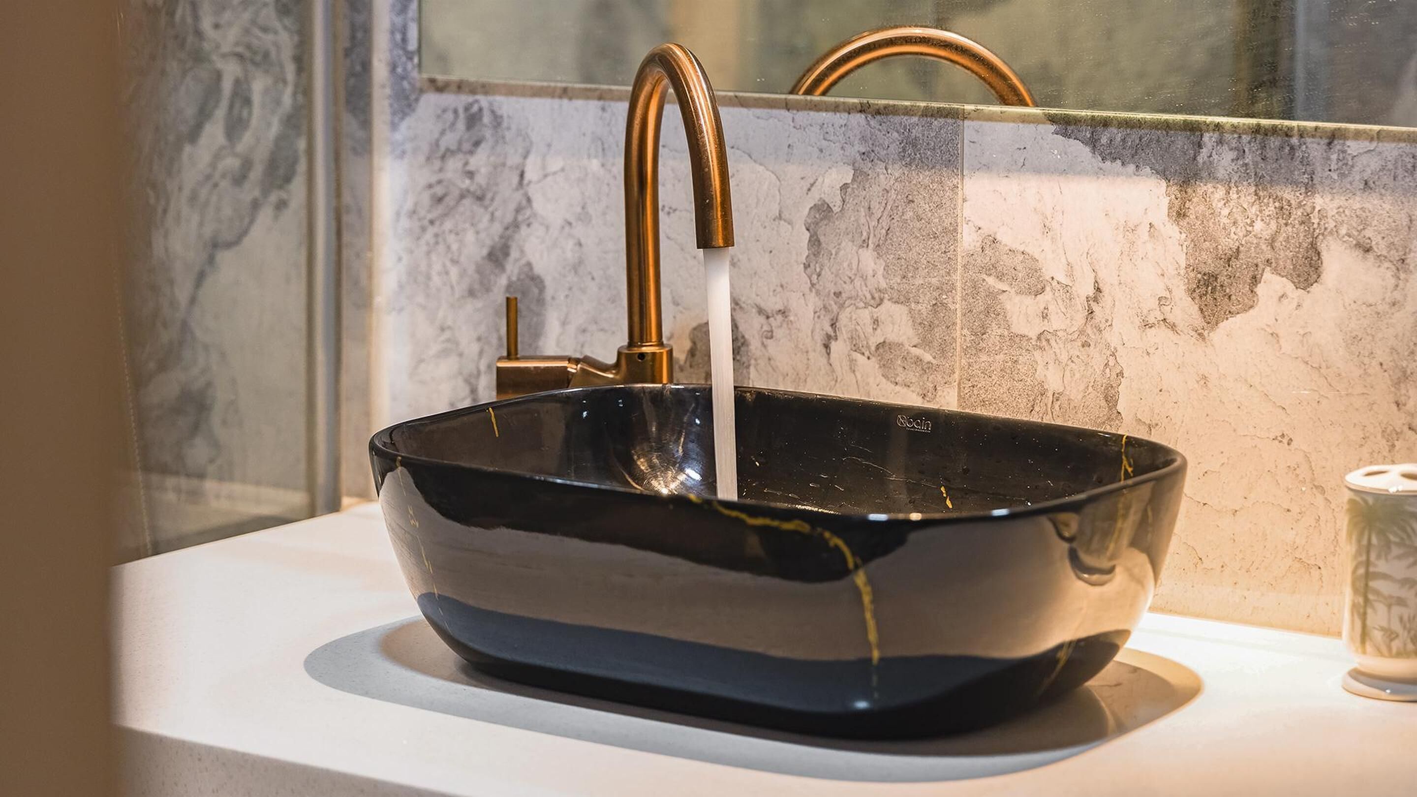 A black basin with a gold faucet on a white countertop.