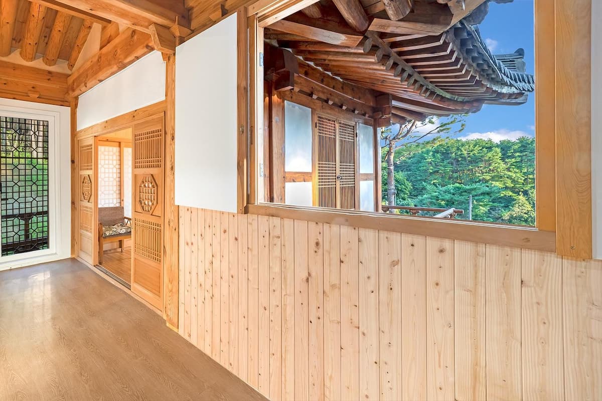 Un pasillo interior de madera con una puerta corredera tradicional japonesa y una ventana que ofrece vistas a la vegetación.