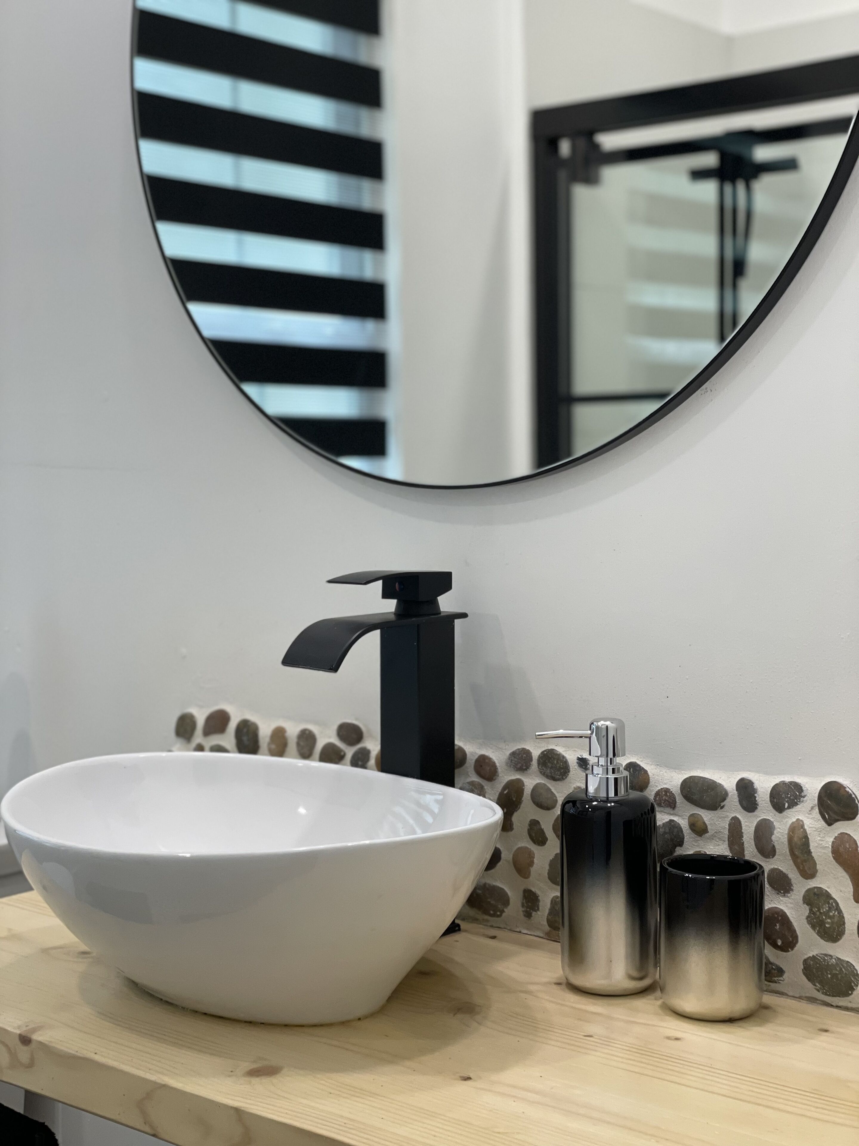 A bathroom with a white sink, black faucet, and two metallic containers on the counter.